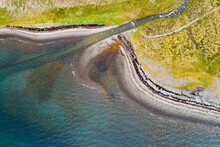 Abstract Aerial View Of Small Stream Flowing Into A Fjord At A Stony Beach With Colorful Seawood, Arnarfjordur, Westfjords