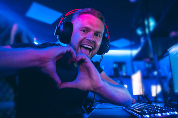 Happy professional cyber sport gamer playing online computer game with headphones, Blurred Red and Blue background