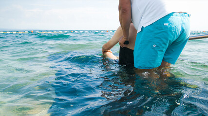 Wall Mural - Disabled man at beach swimming on a wheelchair with assistance help on an accessible ramp.