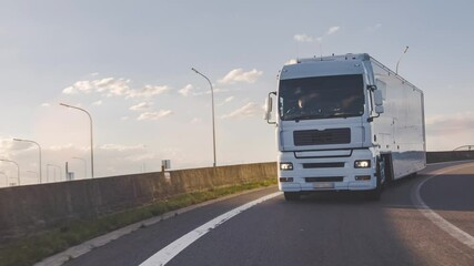 Wall Mural - Cargo truck with cargo trailer driving on a highway. White Truck delivers goods in early hours of the Morning - very low angle drive thru close up shot.