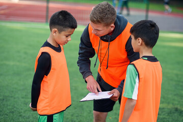 Professional soccer coach tells the strategy of football game to his attentive teen players at stadium during training.