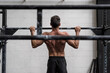 © Guille Faingold/Stocksy - Man doing pull-ups in a gym. view from behind