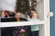 © Rob and Julia Campbell/Stocksy - Young family looking outside through window in winter.