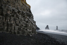 Black Sand Beach With Basalt Formations In Reynisfjara, Iceland. Jagged Rocks Jutting Out Of Sea In Distance