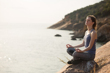 Young woman meditating on the rock near to seaside.