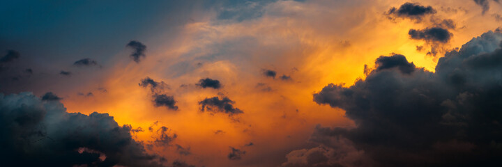 Wall Mural - wide panoramic view of the dramatic post-thunderstorm sky with dark cumulus clouds and orange back light from evening sunset. picturesque artistic background for atmospheric design, decoration