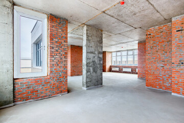 A penthouse apartment room with the bare brick walls in new residential building under construction. The interior of an unfinished big flat without finishing