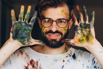 Artist with painted hands. Portrait of a creative painter creating paintings in his home studio with his hands and paint