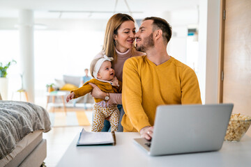 Wall Mural - Mother playing with her kid while dad is working on a laptop.