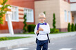 a schoolboy boy with blond glasses with a backpack and a white book is standing at the school. Space for text. Day of knowledge