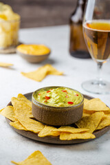 Wall Mural - Nachos chips in a bowl with sauces guacamole and beer over white stone background.