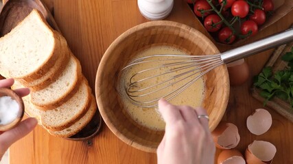 Wall Mural - Whisking eggs with salt in a bowl to prepare breakfast omelette or scrambled eggs. Top view. Woman cooking POV