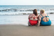 © DisobeyArt - Plus size women sitting on the beach having fun during summer vacation - Rear view of curvy female laughing together - Overweight and diverse body concept