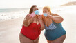 © DisobeyArt - Curvy women friends taking selfie with phone camera on the beach while wearing face mask for coronavirus spread prevention - Summer and people healthcare concept