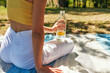 Rear view of a pretty young woman enjoying drink the lemonade while resting in the park on sunlight. Back view of female sitting during picnic having a detox fresh drink.