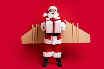 Poster - Full length photo of retired excited grandpa white beard jetpack hands hold box newyear fast delivery children wear santa x-mas costume coat spectacles headwear isolated red color background