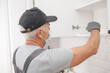 © Parilov - Kitchen installation, worker in medical mask assembling furniture white carved cabinet front
