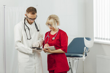 Male and female medical doctors using a tablet and write something and a notebook in a hospital office. Doctors in uniform, man and woman in a gynecological office