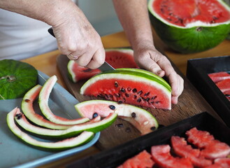 Watermelon Fruit Chips. An elderly woman's hands cut a watermelon into slices for drying. Black grill from home dryer for vegetables and fruits.