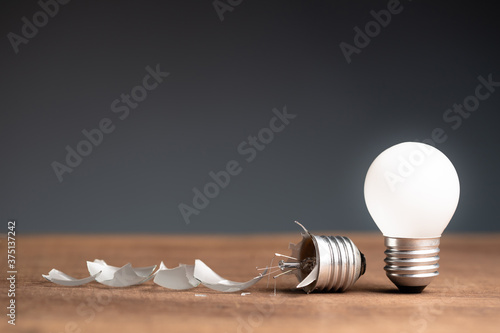 Fotomural Glowing small light bulb and the broken one on the table, concept of fail and su