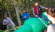 Emotional bearded young man sitting astride big inflatable rodeo bottle, having fun with friends in outdoor amusement park