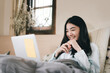 © dodotone - Young adult asian woman relax lying on bed using laptop computer