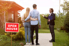 Confident Real Estate Manager Showing Open House To Young Couple Outside