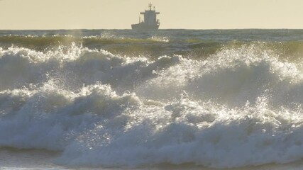 Wall Mural - Sea waves rolling toward beach and sailing cargo ship on sunrise