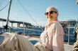 © Artem Varnitsin - Elegant mature woman wearing eyeglasses on a private yacht and looking straight at a camera. Smiling female sitting on a sailboat and enjoying a vacation.
