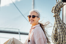 Portrait Of A Happy Mature Woman Wearing Sunglasses On A Yacht. Beautiful Female With Long Hair Looking At Camera While Enjoying A Boat Trip.