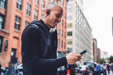 Cheerful ethnic man texting on phone listening music