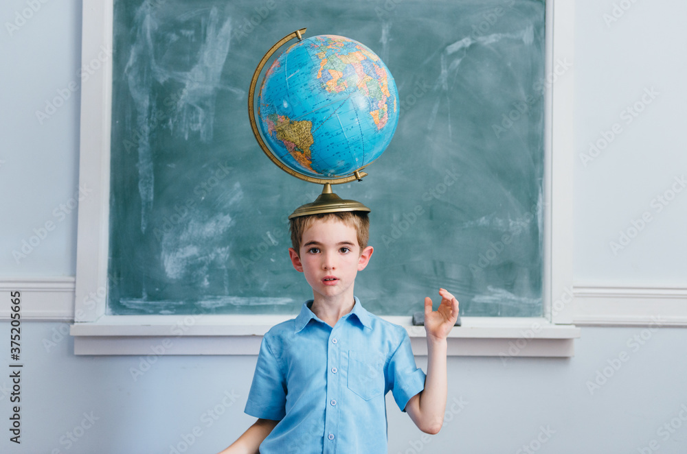 Boy in a classroom balances a globe on his head Stock Photo | Adobe Stock