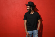 Smiling Handsome Attractive Young African American Man Guy With Dreadlocks 20s Wearing Black Casual T-shirt Hat Posing Looking Aside Isolated On Bright Red Color Wall Background Studio Portrait.