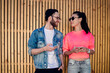 © BullRun - Cheerful millennials dressed in trendy streetwear enjoying live communication during time for blogging at urbanity with wooden backdrop, happy male and female friends discussing text content