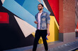 © BullRun - Caucasian male student with education textbooks walking near colorful wall and using 4g wireless internet for mobility, millennial blogger in optical spectacles for vision protection and denim jacket