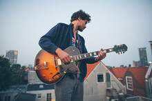 Creative Musician Playing Guitar Outside On A Rooftop Of A Building.