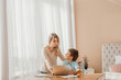 © yana_novak22 - Warm-toned portrait of young mother talking to son while doing homework together sitting at table in cozy kitchen interior, copy space