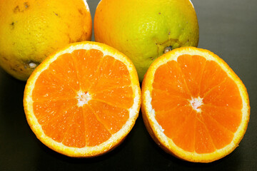 top view of an orange cut in half and 2 whole on a black table. selective focus
