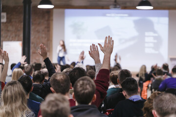 adult students at large conference hall listen to woman speaker and getting hands up for answer on s