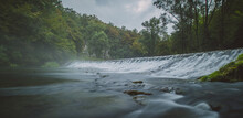Panorama Of River Source Or Spring Of Krupa In Bela Krajina (White Carniola) In Slovenia On A Misty Cloudy Day. Foggy Green River With Rock Formation In The Background And Fast Water Flowing Over A Lo