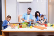 © gorynvd - Mother, father and two sons preparing healthy vegetarian breakfast with fresh vegetables on cozy home kitchen.