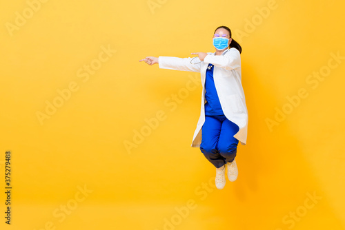 Asian female doctor wearing medical mask jumping and pointing hands to empty spa Poster Mural XXL