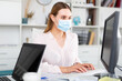 © JackF - Focused young woman in disposable face mask working in business office using laptop