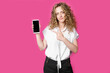 © Dzmitry - Look at this cell phone. Contented happy woman, pointing her index finger at a blank screen, shows a modern device. Isolated on a pink background.