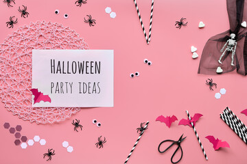 Hexagon confetti, paper drink straws, bats, sugar hearts and spiders. Pink Halloween background, top view, text Halloween party ideas.