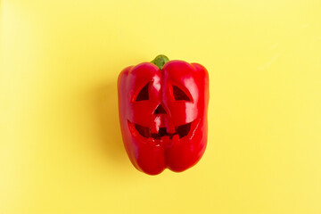 Scary face carved on red bell pepper for Halloween on yellow background. 