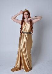 Wall Mural - Full length portrait of girl with red hair wearing long grecian toga and golden wreath. Standing pose iisolated against a grey studio background.