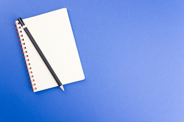 Wall Mural - Closeup of a notebook and a pencil isolated on a blue background