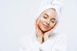 © VK Studio - Studio shot of relaxed beautiful woman with closed eyes tilts head, touches skin gently, applies face cream, wears bath towel on head after taking spa procedures, enjoys facial treatments, body care
