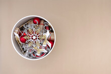 White Round Box With Christmas Decorations In Red, White, Gold And Silver On A Beige Background.
